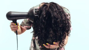 Woman makes herself curly hairstyle. Girl using a modern hairdryer.